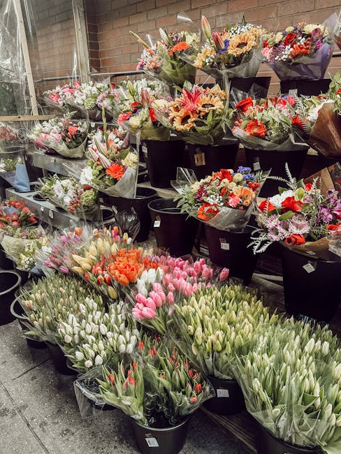 An array of fresh flower bouquets arranged in black buckets inside a floral shop, showcasing a variety of flowers including tulips, roses, chrysanthemums, and lilies in colors such as pink, white, ora